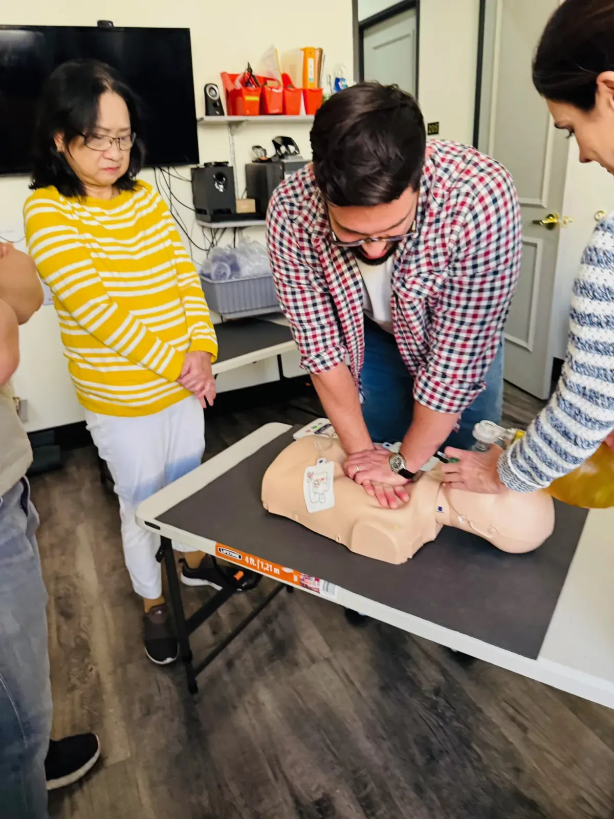 A student practicing adult CPR chest compressions on a manikin while a classmate observes during a Heartbeat Haven BLS skills station